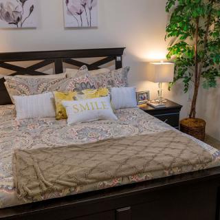 A cozy and well-decorated bedroom with a neatly made bed, featuring multiple pillows and a warm blanket, accompanied by stylish bedside lamps and an indoor plant.