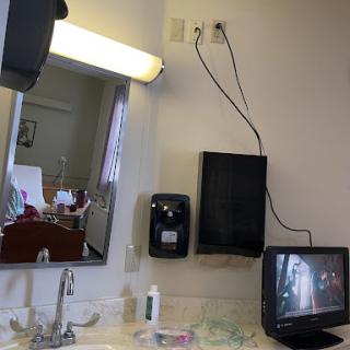 A room featuring a sink area with a mirror, television, and various hygiene products.