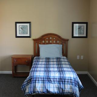 A cozy bedroom featuring a single bed with a plaid blanket and framed wall art.