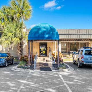 A bright entrance with a blue dome, surrounded by palm trees and a spacious parking lot.