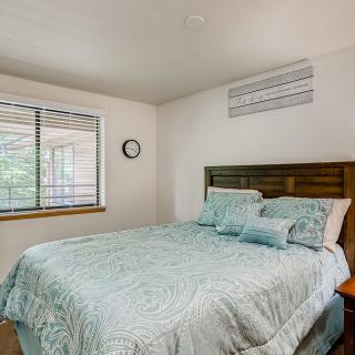 A cozy bedroom featuring a neatly made bed with blue bedding, a wooden headboard, and a window with blinds.