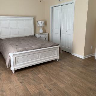 A neatly arranged bedroom with a bed, nightstand, and closet on a wooden floor.