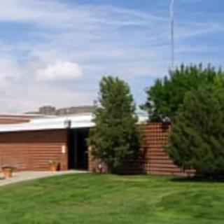A small brick building surrounded by trees and a grassy lawn under a partly cloudy sky.