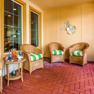 A cozy outdoor patio with wicker chairs and a small side table, featuring decorative accents and a brick floor.