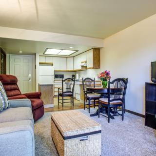 A cozy apartment living room with a sofa, chairs, and a small table, leading to an adjoining kitchen area.