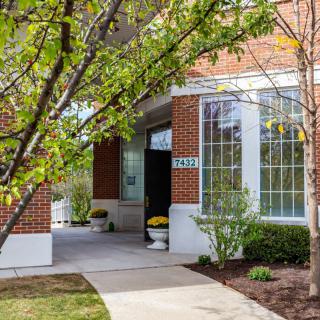 A brick building entrance with large windows and surrounding greenery.