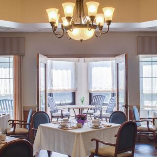 A cozy dining room with a chandelier, set for a meal near large windows.
