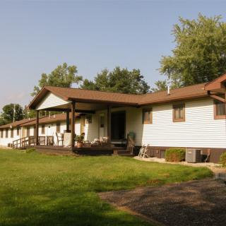 A residential building with a porch and surrounding lawn on a sunny day.