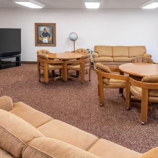 A cozy living room with beige sofas, round tables, wooden chairs, and a television.