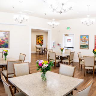 A bright and inviting dining room with elegantly arranged tables, chairs, and floral centerpieces under modern chandeliers.
