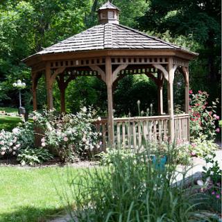 A charming wooden gazebo surrounded by lush greenery and vibrant flowers.