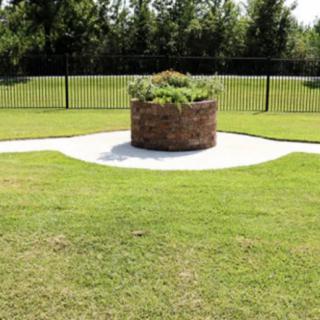 A circular brick planter in the middle of a grassy garden area, surrounded by a fence.