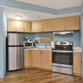 A modern kitchen with wood cabinets, featuring a refrigerator, oven, and microwave.