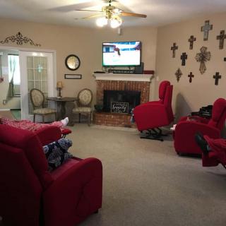 A cozy living room with red recliners, a wall-mounted TV above the fireplace, and numerous cross decorations on the wall.