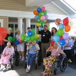 A joyful group of elderly individuals celebrating outdoors with colorful balloons, some in wheelchairs.