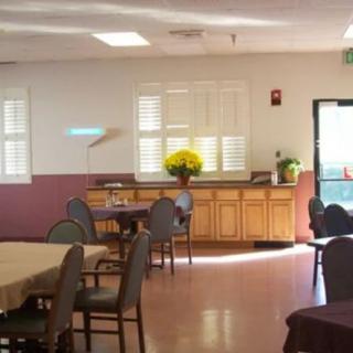 A well-lit dining area with arranged tables, chairs, and a vase of flowers on the counter.
