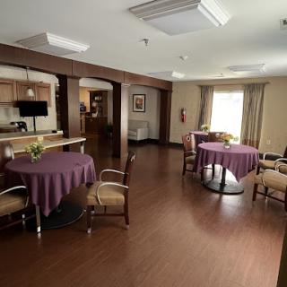 A spacious dining area featuring round tables with purple tablecloths and comfortable seating, illuminated by natural light.
