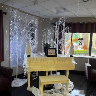 A beautifully decorated lounge area featuring a yellow piano surrounded by festive lighting and decorative trees.