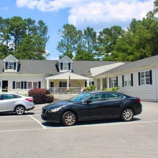 A small parking lot in front of a residential-style building surrounded by trees and a clear sky.