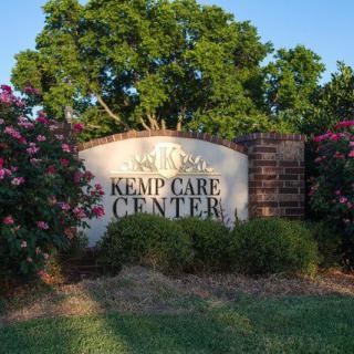 A sign for Kemp Care Center surrounded by flowers and trees.