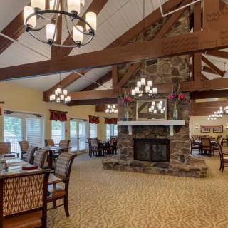 A cozy dining area featuring a large stone fireplace, wood beam ceilings, and elegant chandeliers.