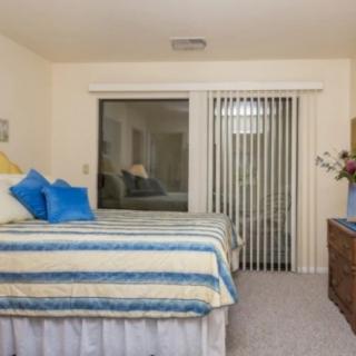 A cozy bedroom with a neatly made bed, decorative pillows, and sliding glass doors with vertical blinds.