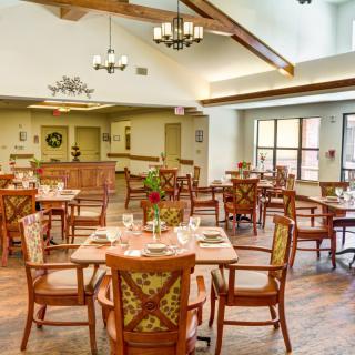 A spacious dining area with wooden tables and chairs, elegantly lit by chandeliers and natural light from large windows.