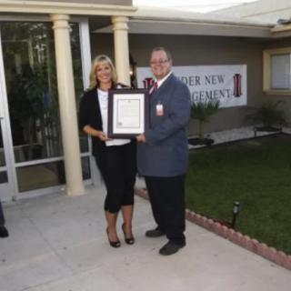 Two people standing outdoors, holding a framed certificate during an award presentation ceremony.