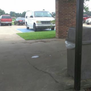 A view of a parking lot featuring a white van and several red cars, with some grass in the foreground.