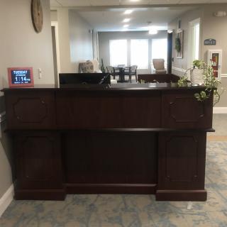 A wooden reception desk in a lobby area with a view of seating arrangements in the background.