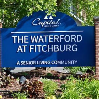 A sign for The Waterford at Fitchburg, a senior living community, surrounded by greenery.