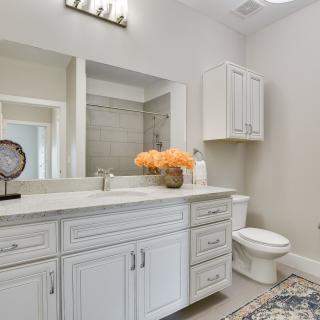 A modern bathroom with a large mirror, white cabinetry, and a vase of flowers on the vanity.