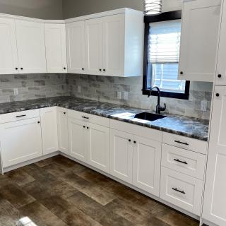 A modern kitchen with white cabinets, granite countertops, and a tile backsplash.