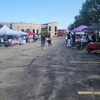 A busy outdoor market with various vendors setting up their tents and customers enjoying the event.