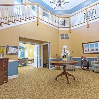 A spacious interior foyer featuring a central table, chandelier, and carpeted floor with surrounding stairs.