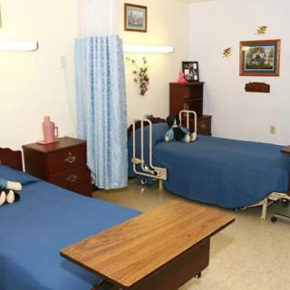 A hospital room with two beds separated by a curtain, featuring bedside tables and simple decor.