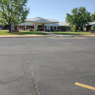 A sunny day view of a well-maintained building surrounded by greenery and a clear parking lot.