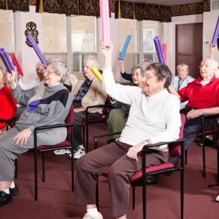 A group of seniors engaging in an indoor exercise class using colorful batons.