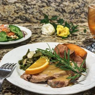 A delicious dinner plate featuring roast meat with orange garnish, vegetables, and a sweet potato, accompanied by a fresh salad and iced tea.