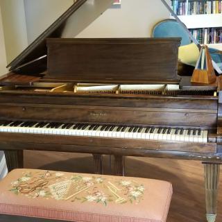 A grand piano with an open lid next to a piano bench and a metronome on top.