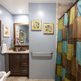 A well-lit bathroom with a mirror, sink, and colorful shower curtain.