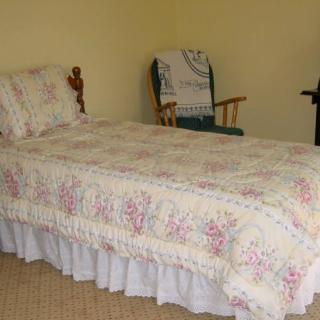 A quaint bedroom with a single bed dressed in floral bedding and a wooden rocking chair in the corner.