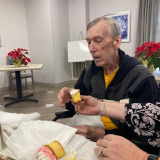 A senior man engaging in an activity with assistance from another person, surrounded by decorative flowers.