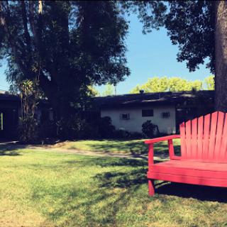 A vibrant red chair sits invitingly on a lush green lawn under clear blue skies.