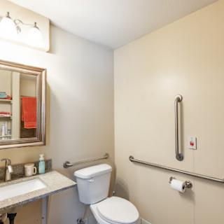 A well-lit bathroom featuring a toilet, sink, and accessible handrails.