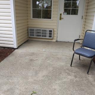 A simple outdoor entrance featuring a chair and a concrete floor.