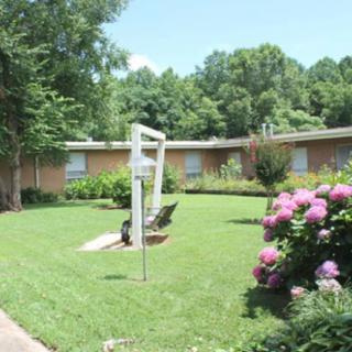 A well-maintained garden with lush green lawn, flowering bushes, and surrounding trees.