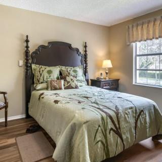A traditional bedroom with a wooden bed, floral bedding, and a nightstand with a lamp by the window.