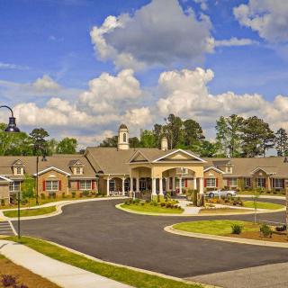 A picturesque view of a residential building with a landscaped driveway and cloudy sky.