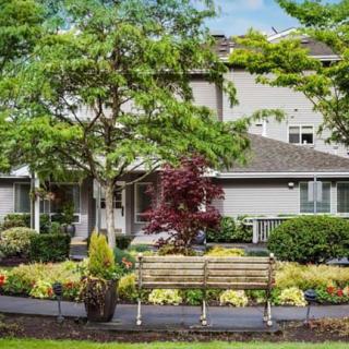 A charming house surrounded by a well-maintained garden with a wooden bench under lush trees.